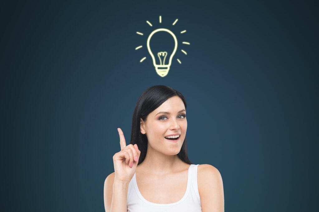 A young woman smiling brightly, pointing upwards towards a glowing lightbulb graphic above her head, symbolizing a bright idea or realization.