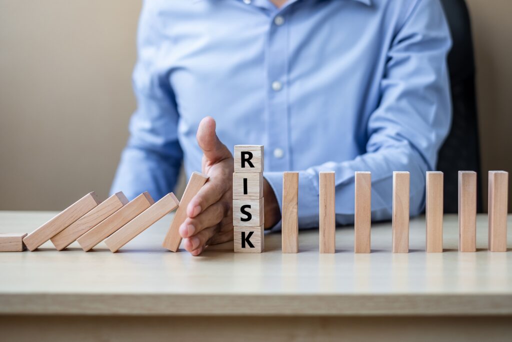 A man in a blue shirt stopping a row of falling dominoes with a block reading "RISK," symbolizing risk management in strategic decision-making.