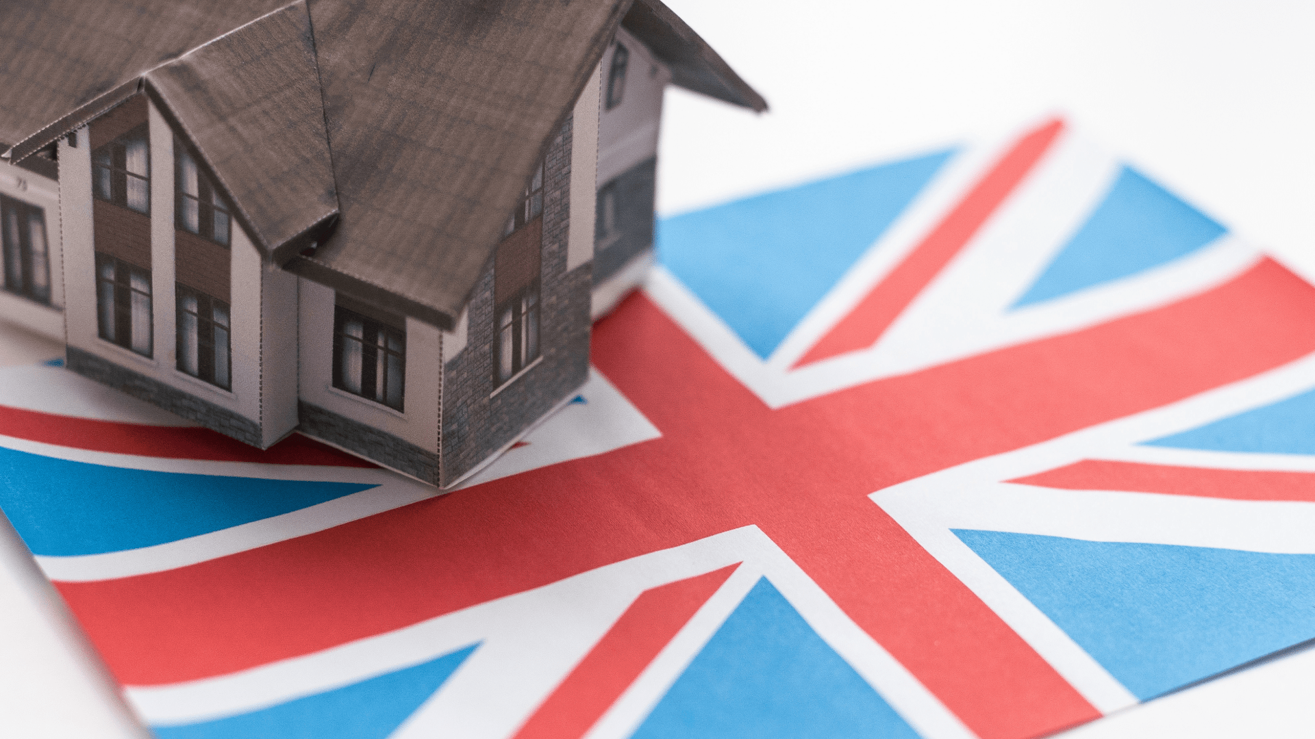 A miniature model of a house resting on a printed Union Jack flag, symbolizing the connection between residential property and national identity in the UK.