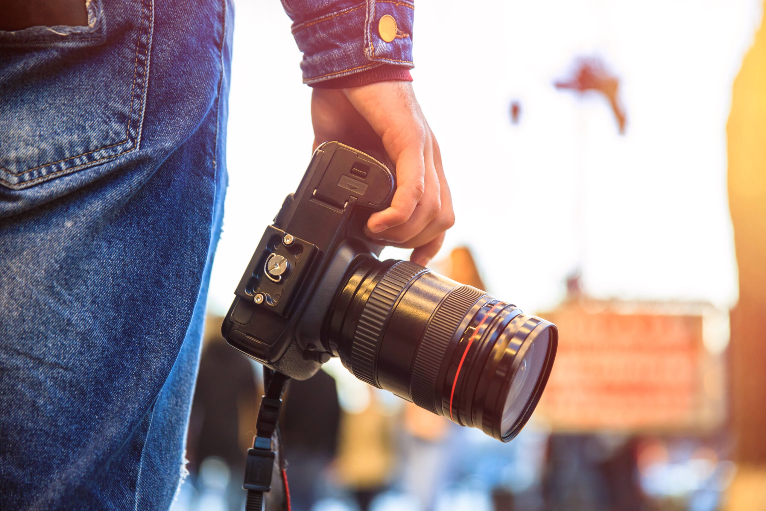 Close-up of a person holding a DSLR camera, wearing a denim jacket and jeans.