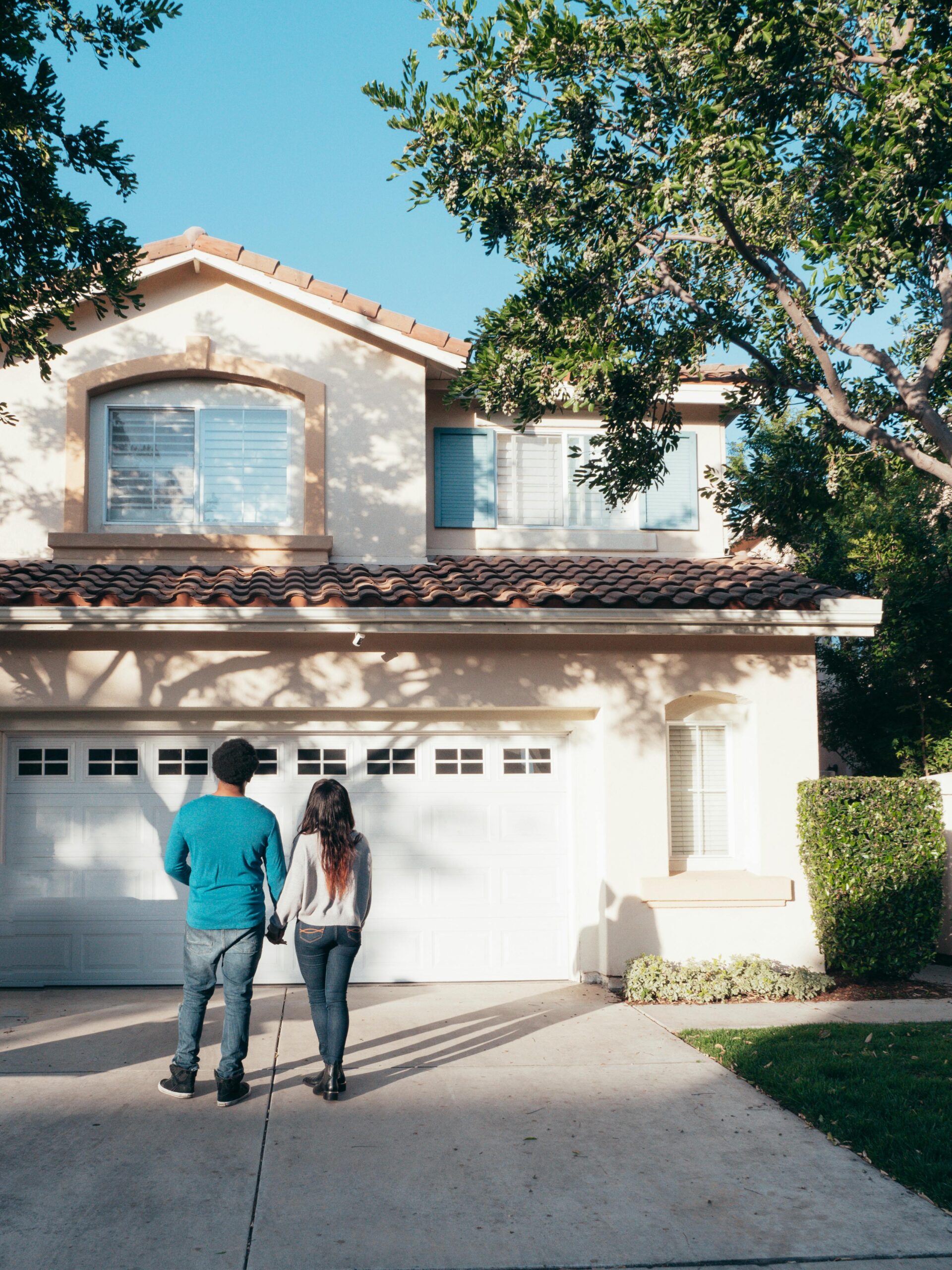 Couple standing hand in hand in front of a modern house with a tiled roof and a double garage.