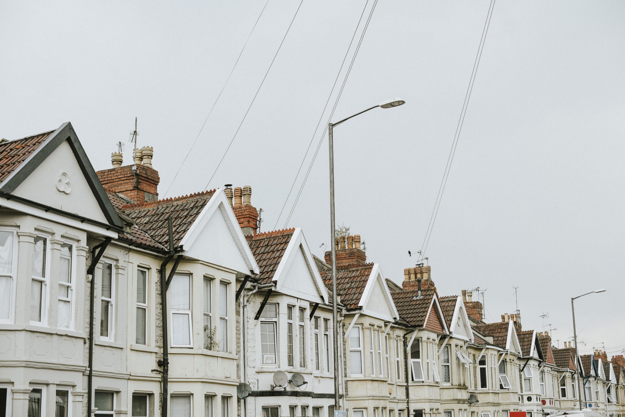 "Row of traditional British terraced houses with red brick chimneys and tiled roofs on a cloudy day"