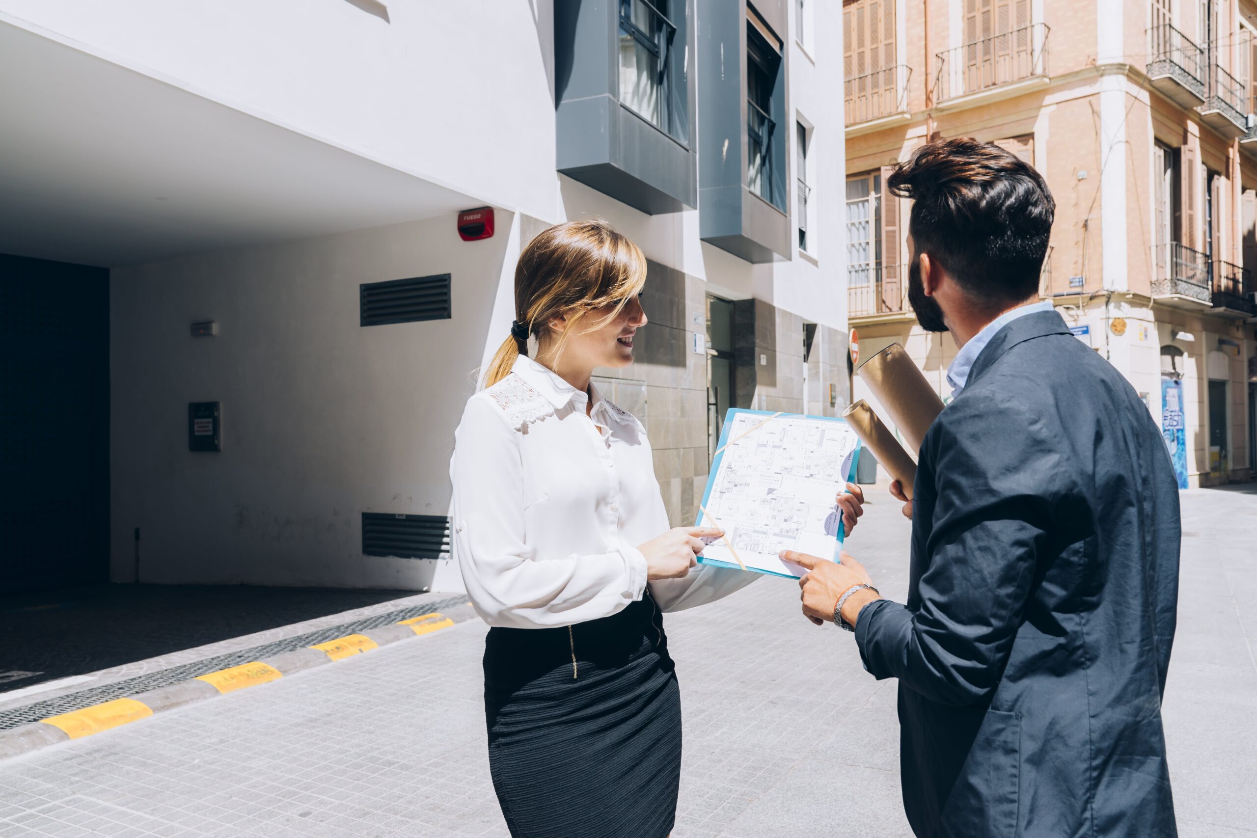 Real estate agent showing property plans to a client outside a building