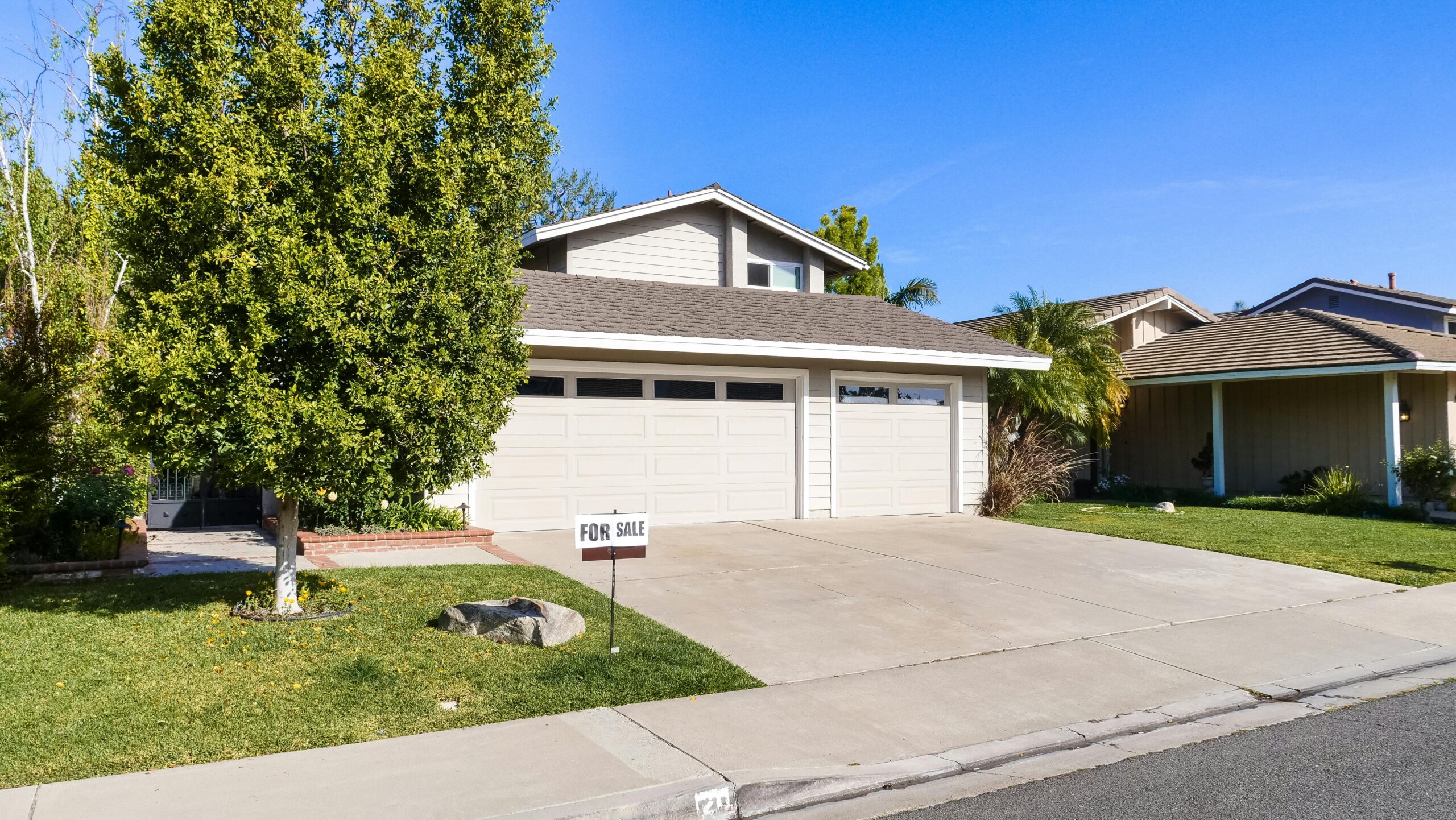 Front view of a two-story house with a large tree and a "For Sale" sign in the front yard.