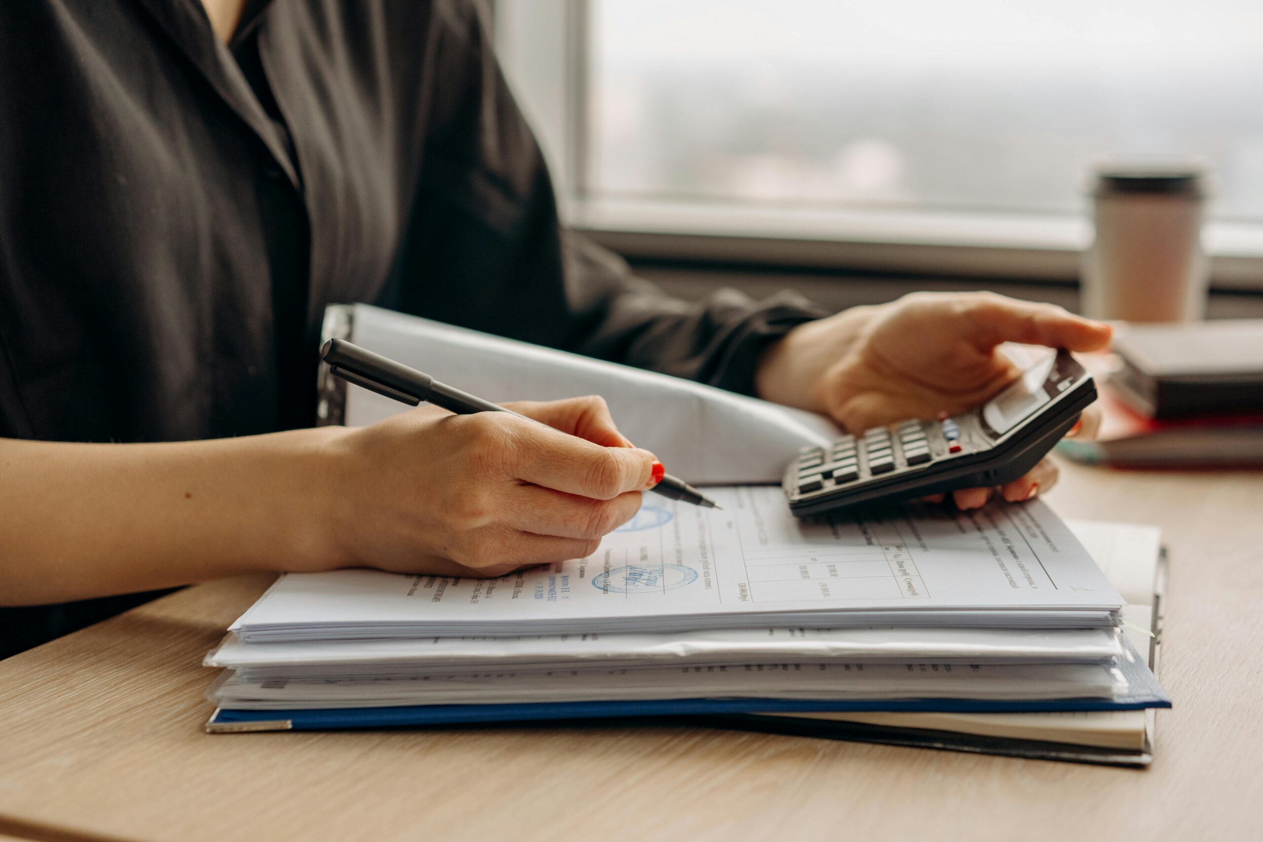 Person using a calculator and reviewing financial documents at a desk.